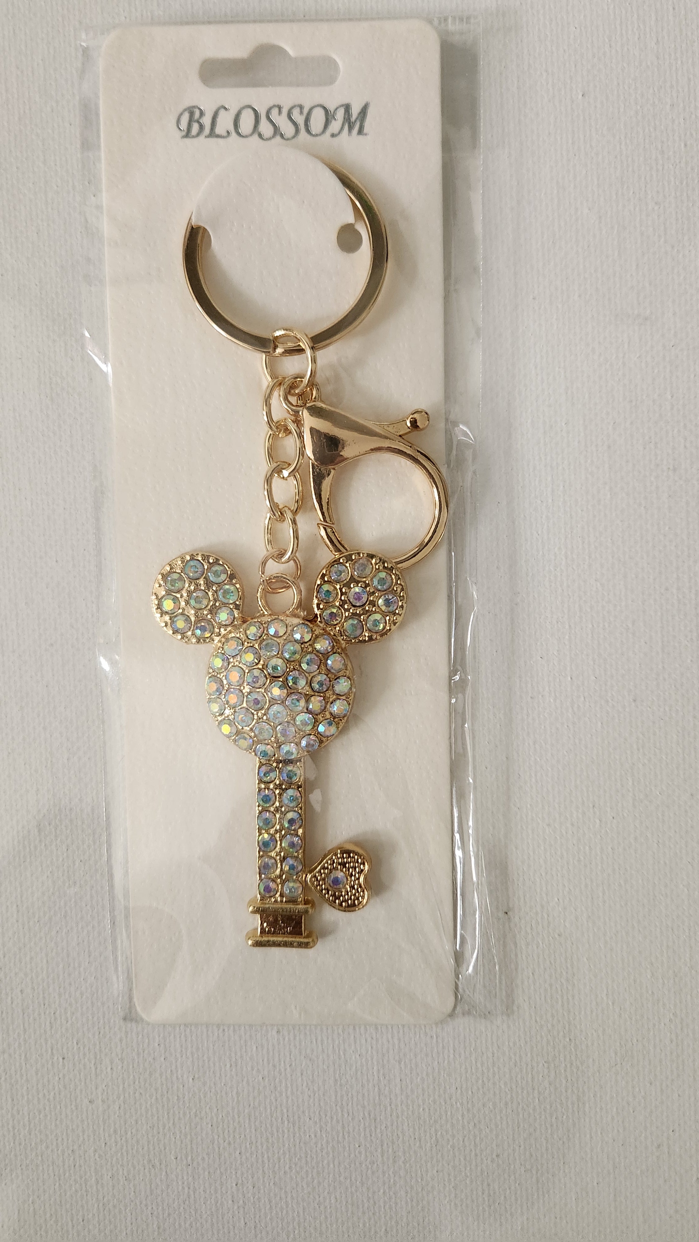 Gold key-shaped keychain with decorative elements on a white card with 'Blossom' branding.